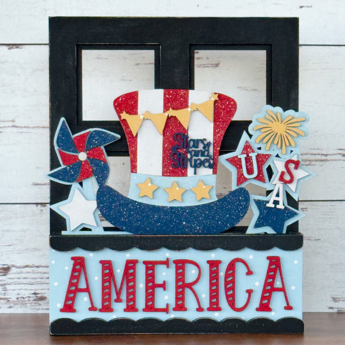 The Rustic Rhode DIY America 2 Piece Insert features a patriotic design with a sparkling Uncle Sam hat, stars, USA, and AMERICA in red, white, blue, and gold—ideal for interchangeable window frames or handmade craft kits.