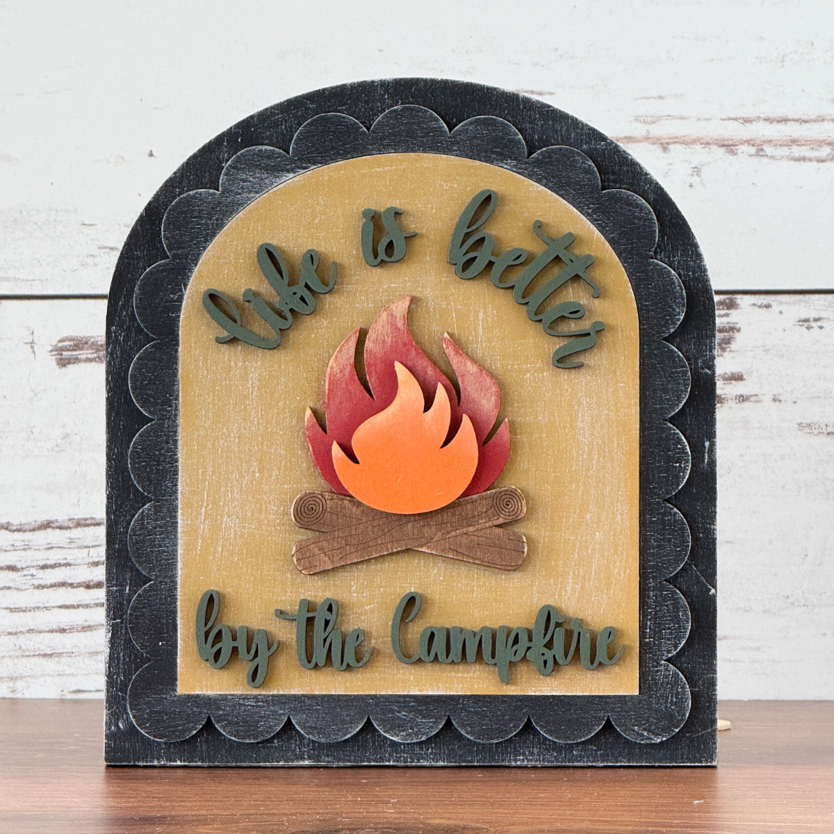 Decorative sign with a campfire design and text on a wooden surface.