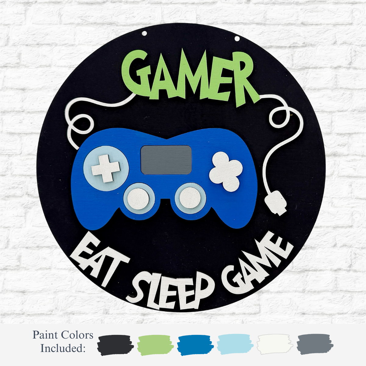 The Rustic Rhodes DIY Gamer Kids Kit features a round sign with a blue game controller, GAMER at the top, and EAT SLEEP GAME at the bottom. Includes gray, green, blue, white, and black paints—perfect for creative kids’ projects.
