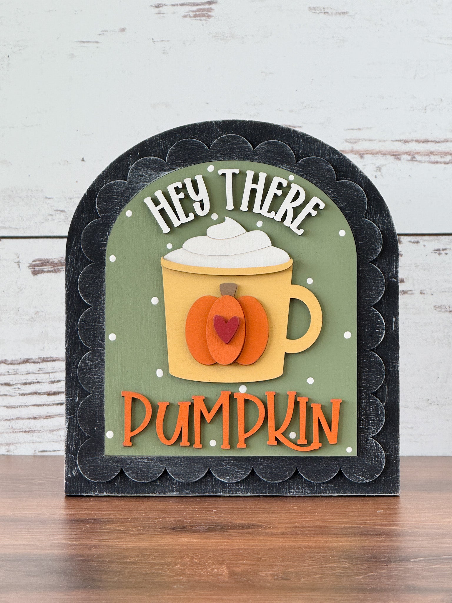 The Rustic Rhode’s DIY Hey There Pumpkin Arch Insert features a mug with whipped cream, a pumpkin design, and playful HEY THERE PUMPKIN text on a green background. This decorative fall sign fits a black scalloped arch insert frame.