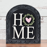 Decorative sign with 'HOME' and heart design on a wooden surface and white wooden background