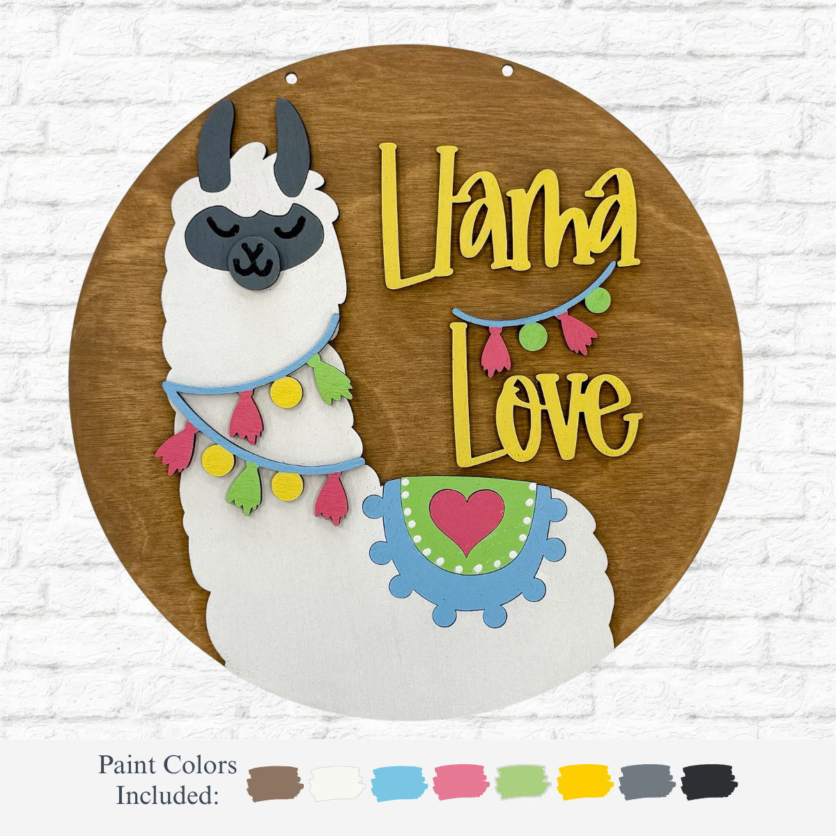 The DIY Llama Love Kids Kit by therusticrhode features a round wooden sign with a smiling white llama, colorful garlands, and a blue blanket with a red heart. “Llama Love” appears in yellow. Includes paint colors for decorating.