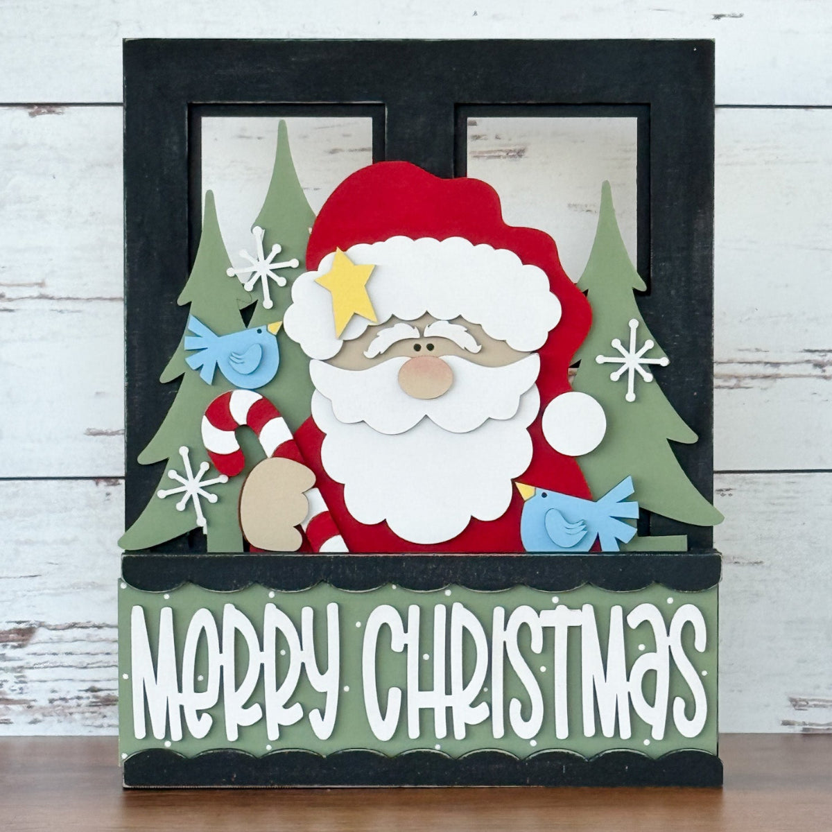 The Rustic Rhode’s DIY Merry Christmas 2 Piece Insert features a cartoon Santa with a candy cane, green trees, blue birds, and “Merry Christmas”—ideal handmade décor for your Interchangeable Window Frame.