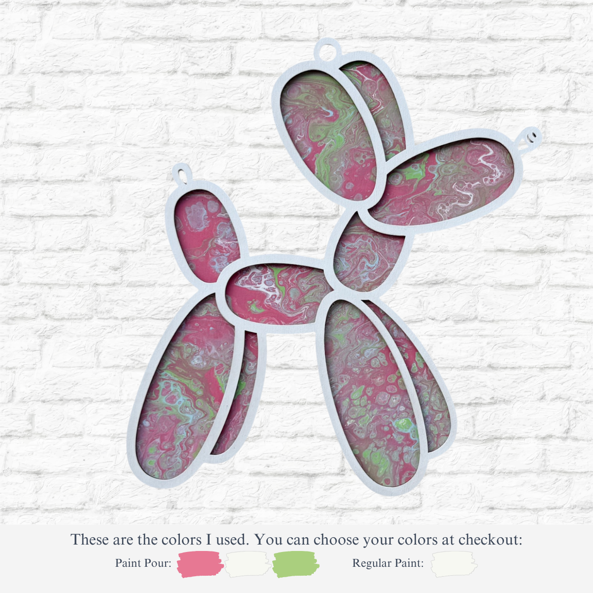 The Rustic Rhodes DIY Paint Pour- Balloon Dog wall art features swirling pink, green, and white paint in each segment, set against a white brick wall. Below are labeled pink and green crafting paint samples for home use.