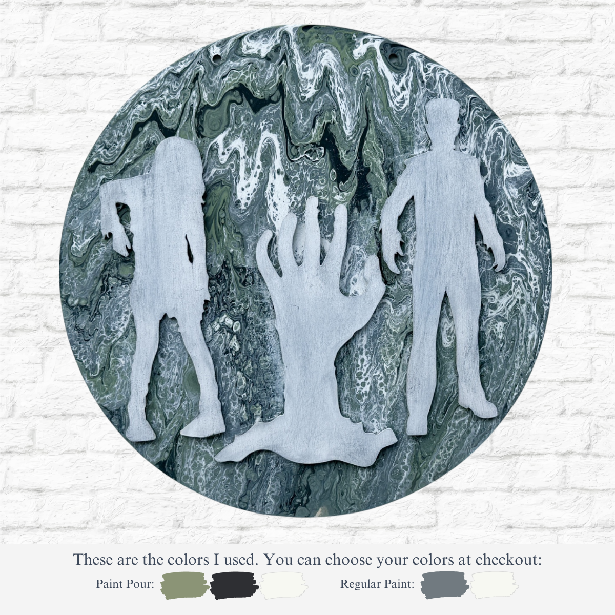 The Rustic Rhode’s DIY Paint Pour- Zombies features spooky zombie silhouettes and a raised hand in light gray on a marbled green, white, and gray circular canvas, with paint swatches shown below against a brick wall.