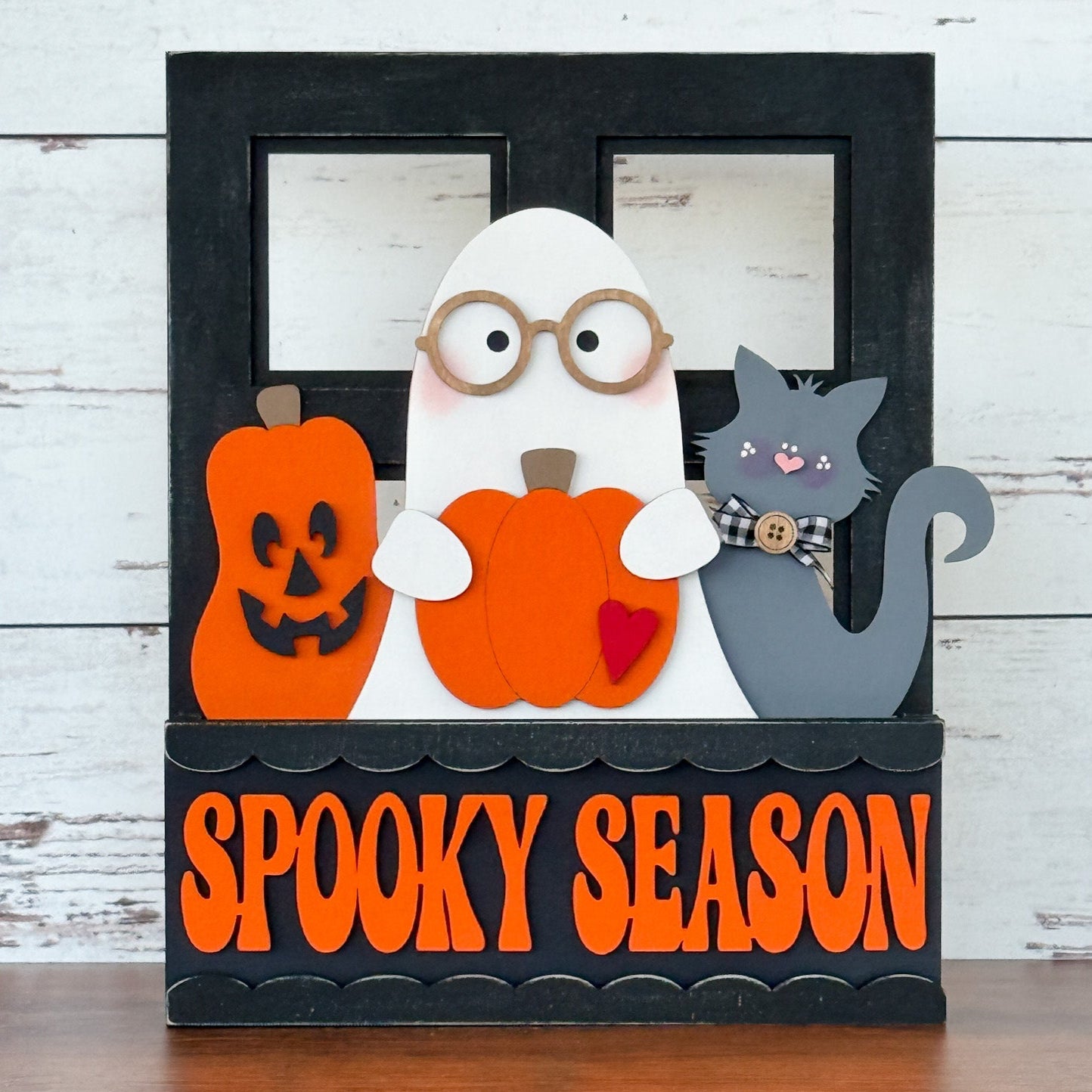 The Rustic Rhode’s DIY Spooky Season 2 Piece Insert is a handmade home décor featuring a ghost with glasses, gray cat with plaid bow, and pumpkins before an interchangeable frame, finished with bold orange Spooky Season lettering.