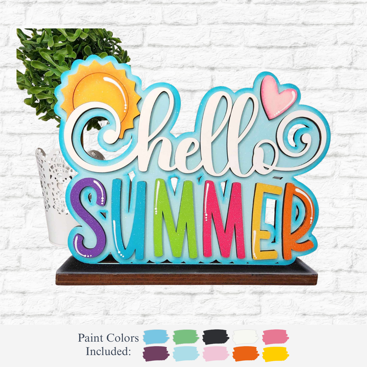 The Rustic Rhode DIY Standing Summer Word Block features hello SUMMER in vibrant, playful letters with a sun, heart, and green plant accents—an ideal summer décor piece. Paint color samples are displayed on a white brick wall backdrop.