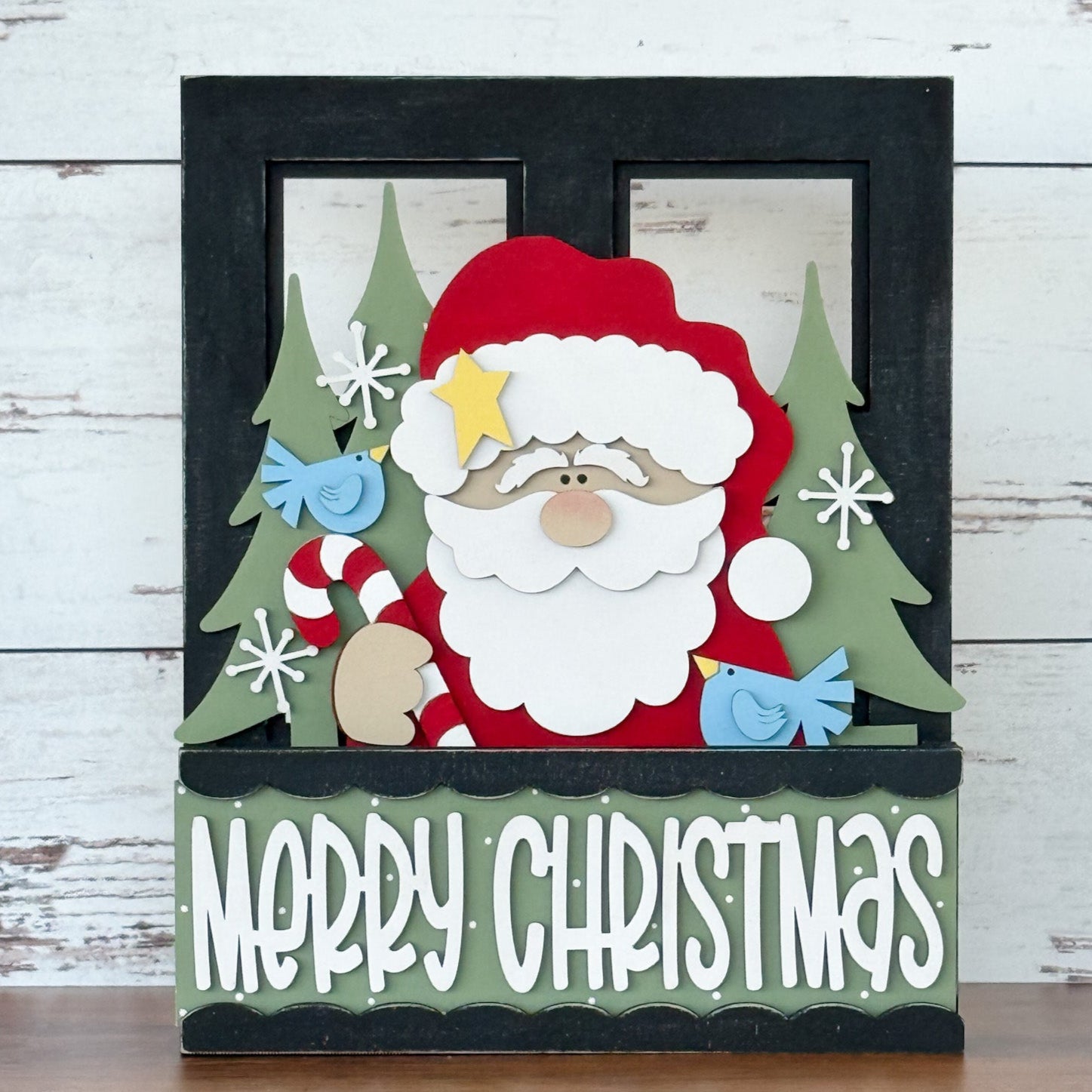 The Rustic Rhode DIY Interchangeable Window Frame features Santa Claus with a candy cane among green trees, blue birds, and snowflakes, with a Merry Christmas sign on a rustic wood background.