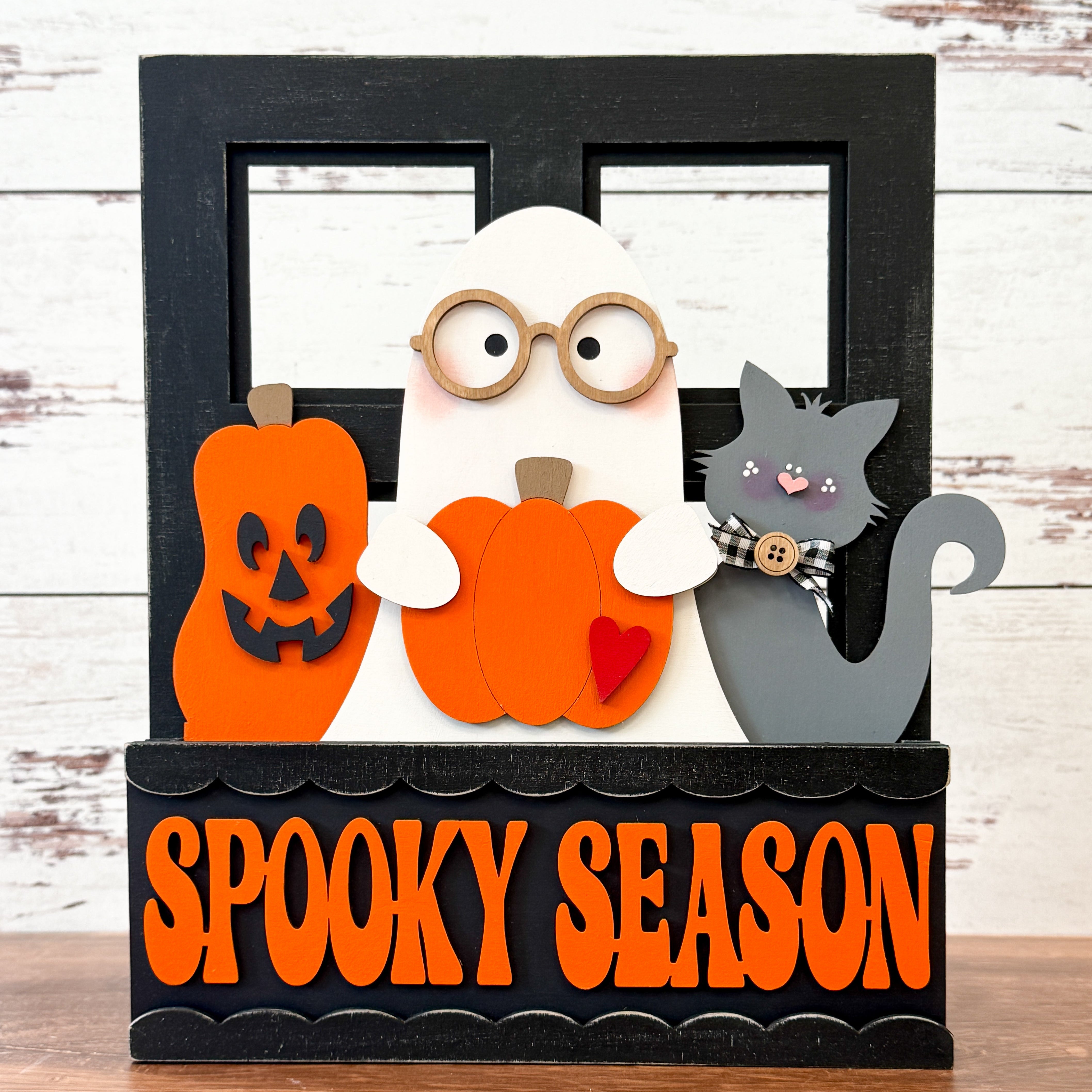 The Rustic Rhode DIY Interchangeable Window Frame features a festive Halloween design with a ghost in glasses, a plaid-scarf black cat, two orange pumpkins, and a SPOOKY SEASON sign.