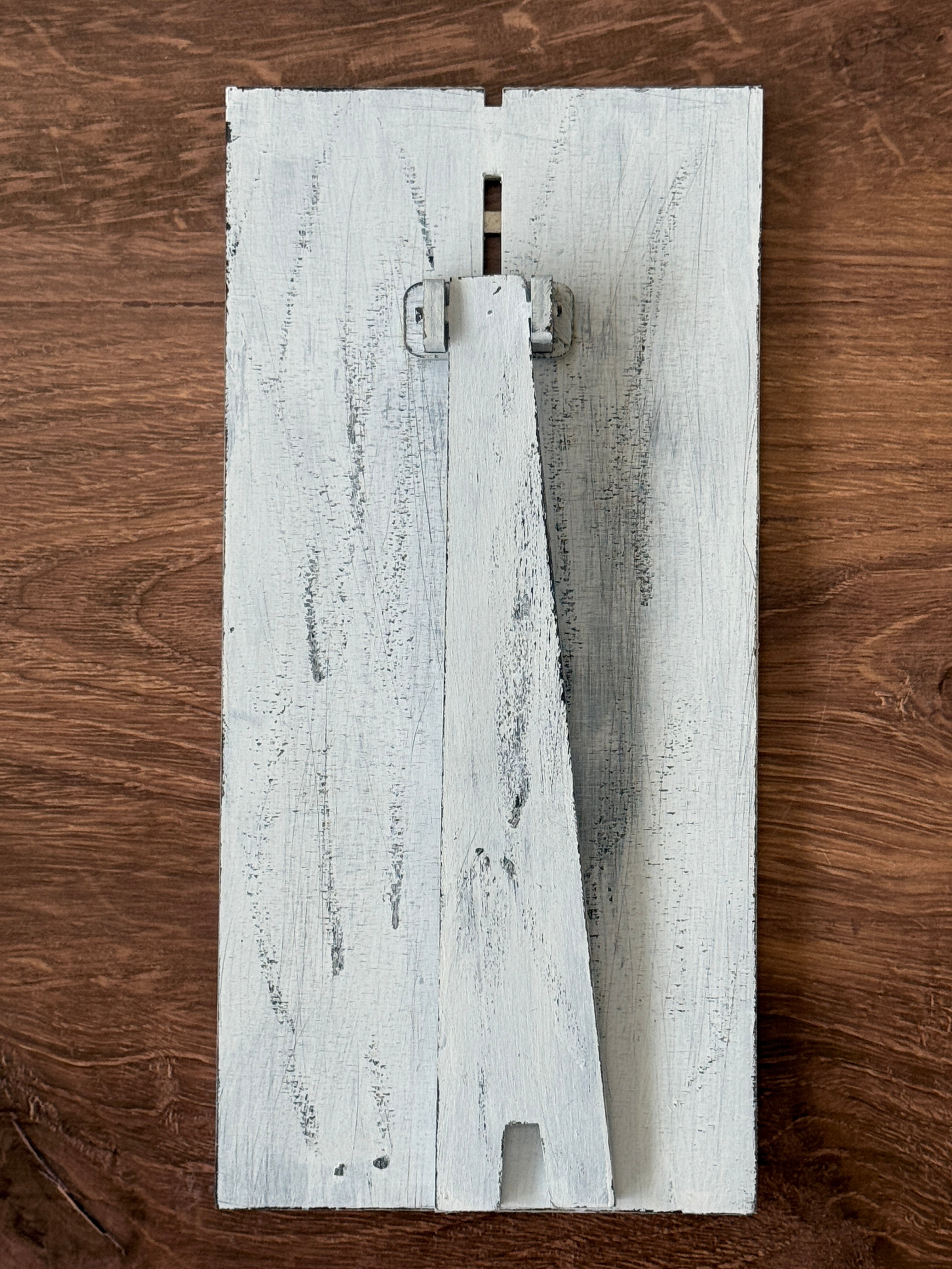 The Rustic Rhode DIY Interchangeable Farmhouse Frame is a distressed white wood piece with a triangular stand, resting on brown wood—ideal for personalized home decor.