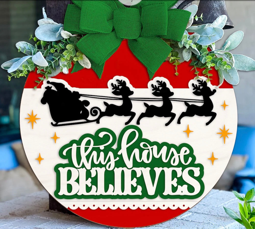 Celebrate the season with The Rustic Rhode's Set The Barre Fundraiser-October 25th: a festive DIY door hanger kit featuring a green bow, greenery, Santa's sleigh silhouette, and "This House Believes" for holiday cheer!.