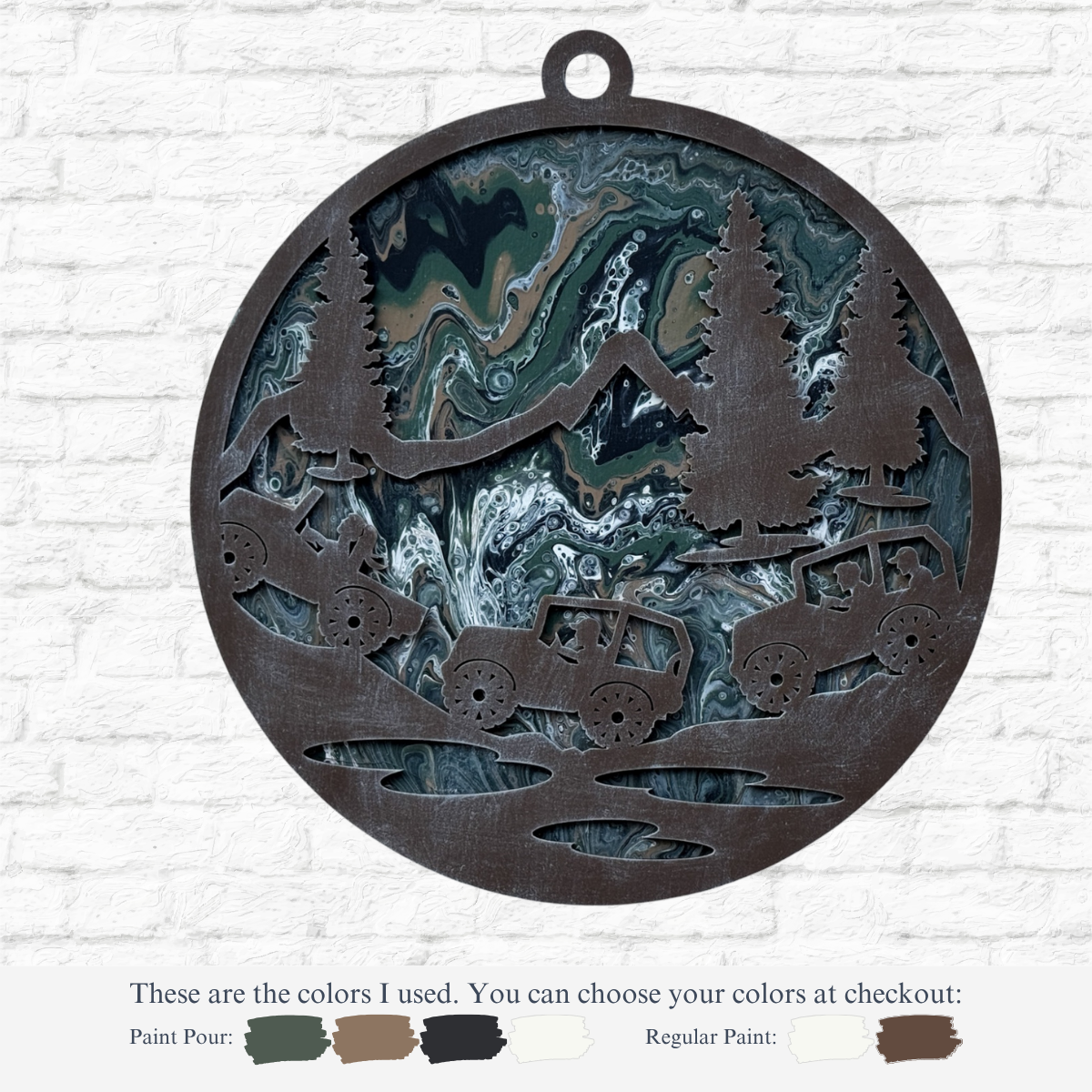 The Rustic Rhode’s DIY Paint Pour – Off Road Mountain features a round metal ornament with cut-out trees, mountains, and off-road vehicles over a swirled green, blue, black, and cream background—ideal for your next craft project. Color details below.