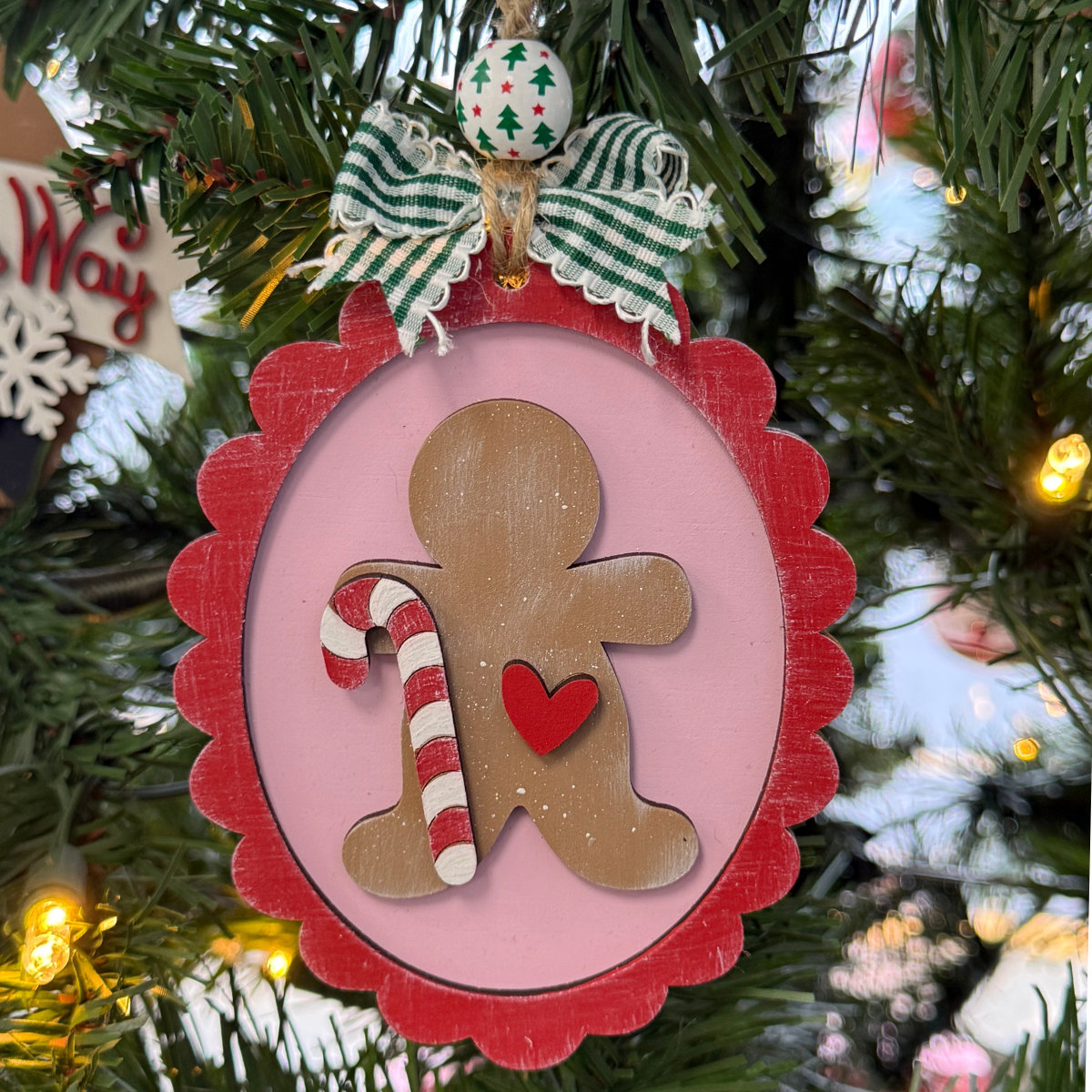 The Rustic Rhode DIY Christmas Baking Gingerbread Ornament features a wooden gingerbread person with a red heart and candy cane, ready to paint or use in craft kits—comes unassembled for fun holiday decorating.