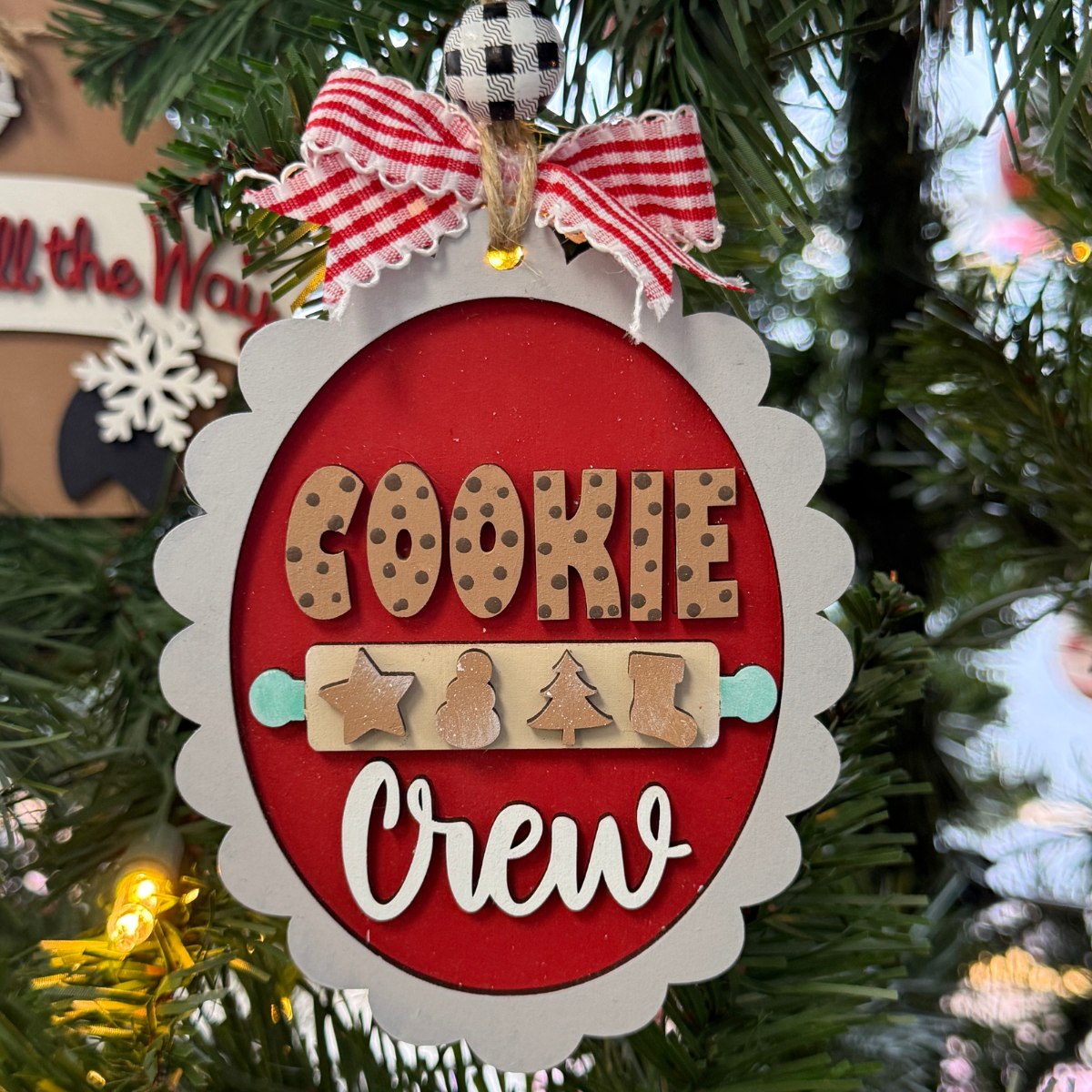 The Rustic Rhode’s DIY Christmas Baking Cookie Crew Ornament has cookie-shaped letters, a red and white scalloped edge, and ribbon with a bow. Perfect for painting or assembling, this kit makes festive décor for your tree.