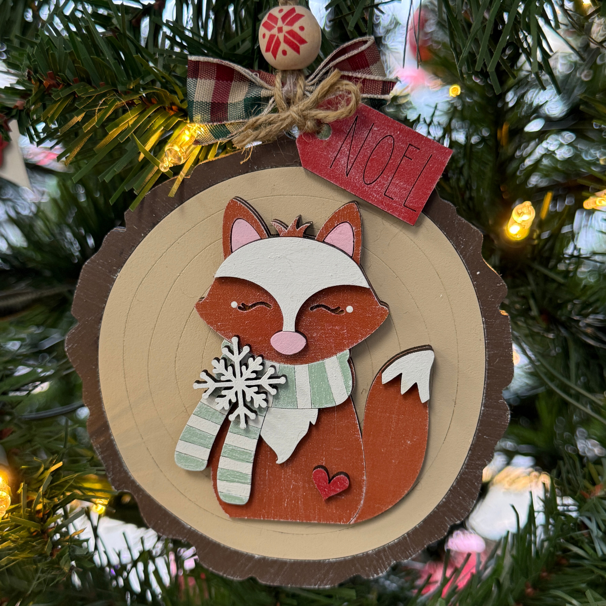 The Rustic Rhode’s DIY Woodland Creatures Ornament- Fox kit includes unassembled pieces to create a fox with a green and white scarf, snowflake chest, plaid bow, and red NOEL tag—perfect for a charming Christmas tree decoration.