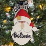 The Rustic Rhode’s DIY Believe In Santa Ornament kit features unassembled pieces to paint yourself, inspired by a Santa ornament with "Believe" on his beard and a plaid bow—perfect for your festive Christmas tree décor.