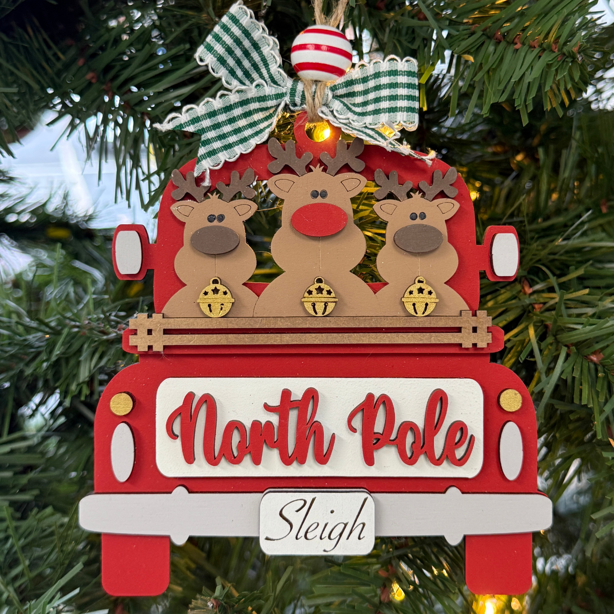The Rustic Rhode DIY Truck Ornament-North Pole Reindeers features a red truck with three reindeer and a green checked bow, perfect for hanging on your tree. Part of our ornament kits collection, it's ready to paint and personalize.