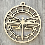 The Rustic Rhode’s M. Mello Suncatcher Workshop-10/7 features a circular wooden ornament with a dragonfly cutout and geometric lattice—perfect as a unique suncatcher or craft display on light wood.