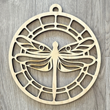 The Rustic Rhode’s M. Mello Suncatcher Workshop-10/7 features a circular wooden ornament with a dragonfly cutout and geometric lattice—perfect as a unique suncatcher or craft display on light wood.