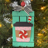 The Rustic Rhode’s DIY Hot Cocoa Pallet Ornament is a to-go cup-shaped Christmas tree kit with a mint candy, ribbon, and “Have a cup of cheer” on teal—perfect for painting and assembling yourself.