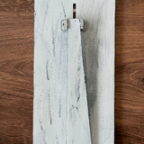 The Rustic Rhode DIY Firefly Interchangeable 4.25 Insert features a distressed white wooden board with a vertical rectangular rotating latch, perfect for farmhouse frames or creative projects, set against a brown wood background.