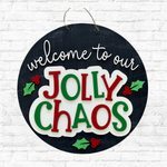 A round black sign with festive accents hangs on a white brick wall—a charming piece from The Rustic Rhode for Cathy's Craft Night, November 13th at 6:00pm, perfect for your holiday decor or as a seasonal door hanger.