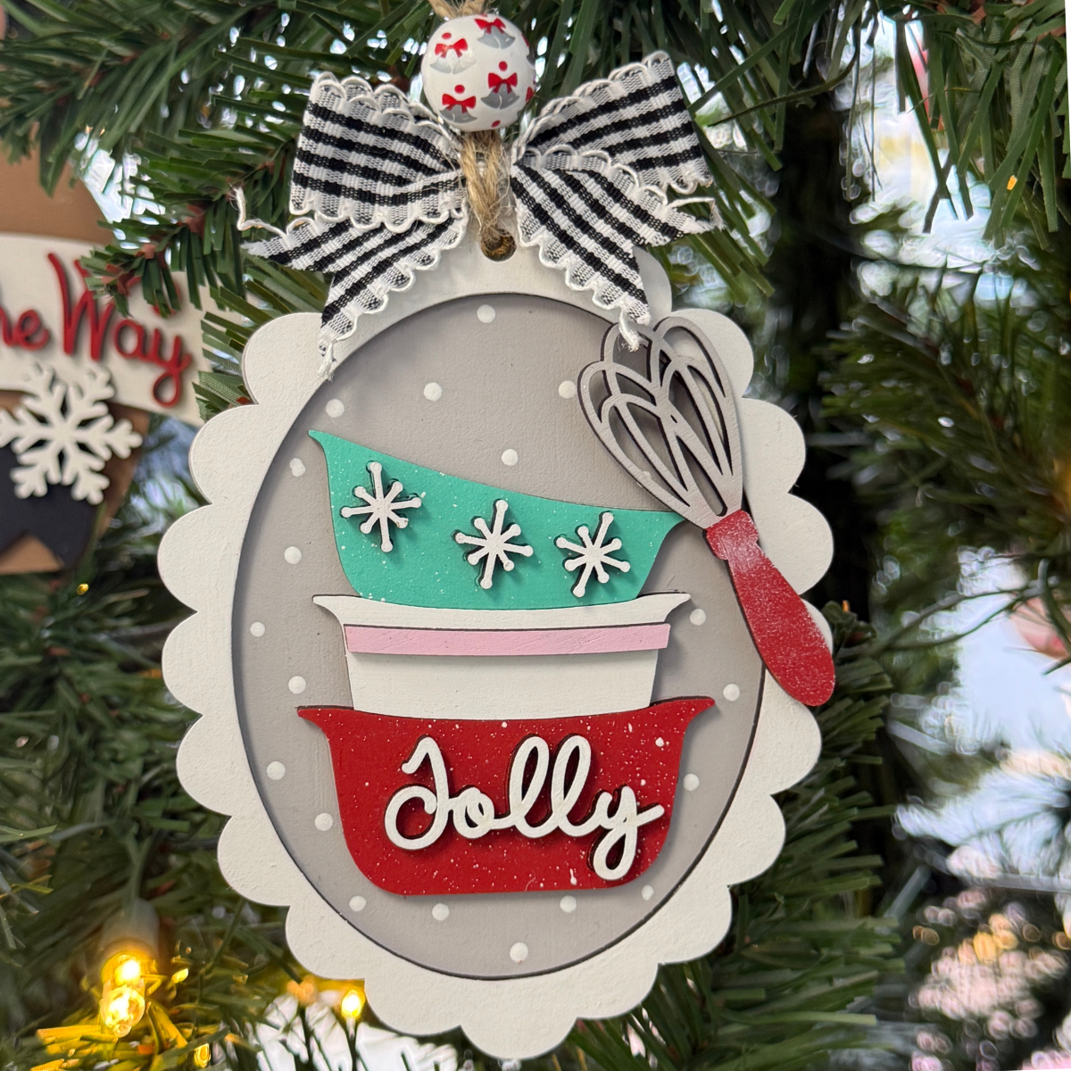 The Rustic Rhode DIY Christmas Baking Bowls Ornament kit includes unassembled pieces featuring stacked retro bowls with "Jolly," snowflakes, a whisk, and gingham bow—ready for you to paint and hang on your tree.