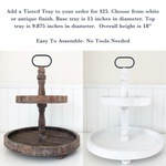 Displayed side by side are two round, two-tiered trays from The Rustic Rhode: one dark wood, one white. Each includes a decorative handle and is perfect for the DIY Hot Cocoa Tiered Tray Kit. No tools needed for assembly.