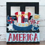 The Rustic Rhode DIY America 2 Piece Insert features a patriotic design with a sparkling Uncle Sam hat, stars, USA, and AMERICA in red, white, blue, and gold—ideal for interchangeable window frames or handmade craft kits.