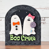 The Rustic Rhode’s DIY Scalloped Arch Insert Frame displays two cartoon ghosts with bows and buttons—one holding a lollipop. Boo Crew is written in green, and the black background with white dots resembles stars.