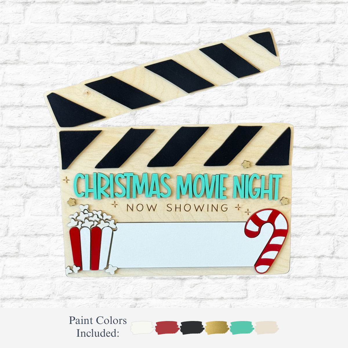 The Rustic Rhode DIY Christmas Movie Night wood clapperboard features “Now Showing” text, popcorn and candy cane graphics—ideal for holiday crafts. Paint color samples are shown below it on a white brick background.
