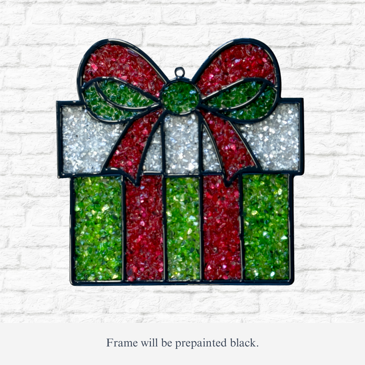 The Rustic Rhode DIY Christmas Present Faux Suncatcher features sparkling red, green, and white details in a gift box shape—perfect for adding festive charm to your holiday décor against any white brick wall.