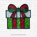 The Rustic Rhode DIY Christmas Present Faux Suncatcher features sparkling red, green, and white details in a gift box shape—perfect for adding festive charm to your holiday décor against any white brick wall.