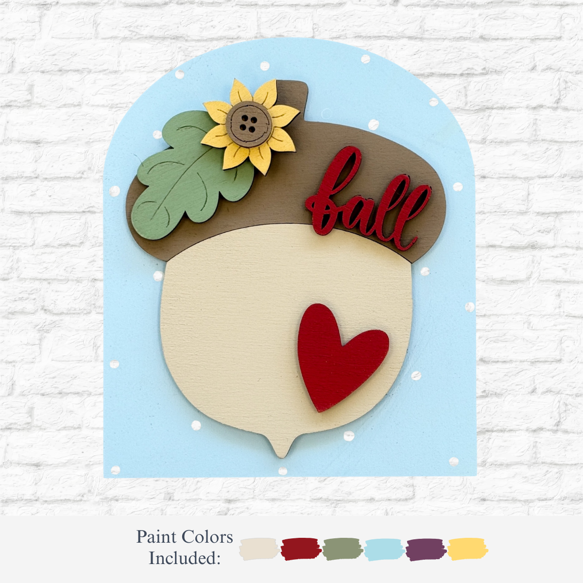 The Rustic Rhode DIY Fall Acorn Arch Insert features a wooden acorn with a sunflower, green leaf, red heart, and fall on a dotted blue background—perfect fall campfire décor. Pairs beautifully with a Scalloped Arch Insert Frame.