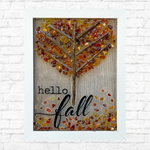 The Rustic Rhode’s DIY Fall Leaves Sea Glass Frame features a tree of twigs and autumn-hued sea glass leaves, plus hello fall on the front. Perfect Halloween décor, it’s shown against a white brick wall.