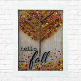 The Rustic Rhode’s DIY Fall Leaves Sea Glass Frame features a tree of twigs and autumn-hued sea glass leaves, plus hello fall on the front. Perfect Halloween décor, it’s shown against a white brick wall.