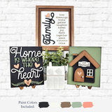 The Rustic Rhode’s DIY Family Home Sign Trio, including a ceramic house, is displayed against a white brick wall. The black, white, and pastel signs show family phrases with four paint swatches below to inspire customizable home decor.
