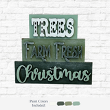 The Rustic Rhode DIY Farm Fresh Christmas Word Stacker features green wooden signs reading TREES, FARM FRESH, and Christmas in various fonts, shown with four paint swatches—a perfect farmhouse holiday décor piece against a white brick wall.