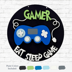 The Rustic Rhodes DIY Gamer Kids Kit features a round sign with a blue game controller, GAMER at the top, and EAT SLEEP GAME at the bottom. Includes gray, green, blue, white, and black paints—perfect for creative kids’ projects.