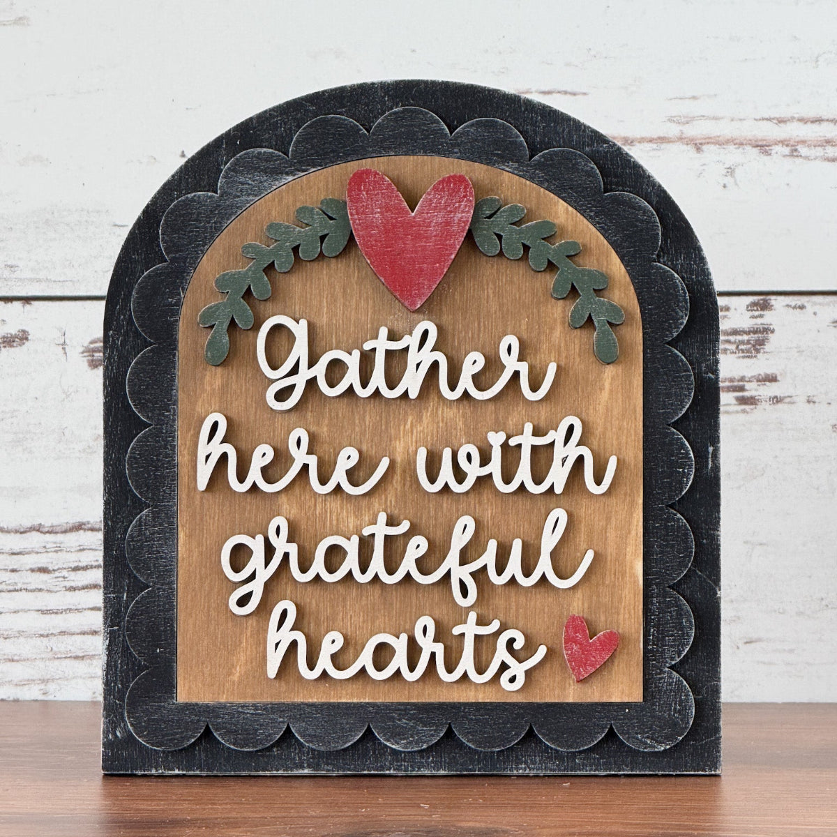 Decorative sign with 'Gather here with grateful hearts' text and red hearts on a wooden surface.