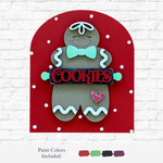 The Rustic Rhode’s DIY Gingerbread Cookie Arch Insert features a smiling gingerbread with a green bow tie and COOKIES sign. Includes festive paint colors—green, brown, red, black, and white—great for your holiday craft kit!.