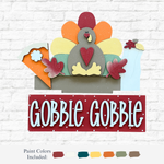 The Rustic Rhode’s DIY Gobble Gobble 2 Piece Insert features a colorful wooden turkey, pie, leaves, vase, and GOBBLE GOBBLE on a red panel—paint included. Perfect handmade Thanksgiving décor for your home!.