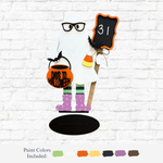 The Rustic Rhode’s DIY Halloween Countdown Ghost features glasses, holds a “31” chalkboard, a pumpkin bucket labeled “Days to Halloween,” and a candy bucket. It stands on a black oval base perfect for your festive décor.
