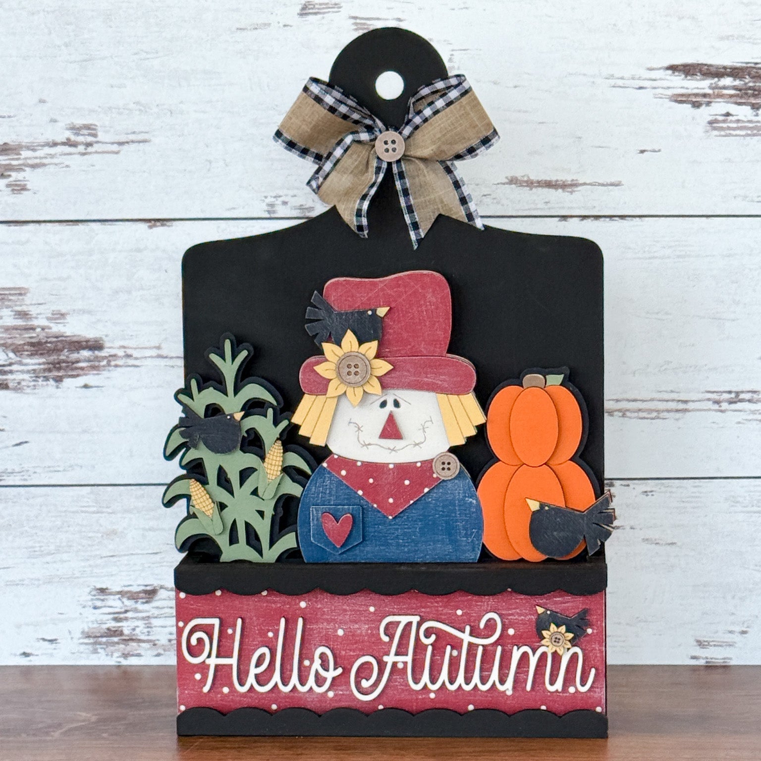 The Rustic Rhode DIY Hello Autumn 2 Piece Insert features a scarecrow, pumpkins, corn stalks, blackbirds, and a plaid bow—a charming handmade fall decor or interchangeable window frame insert.