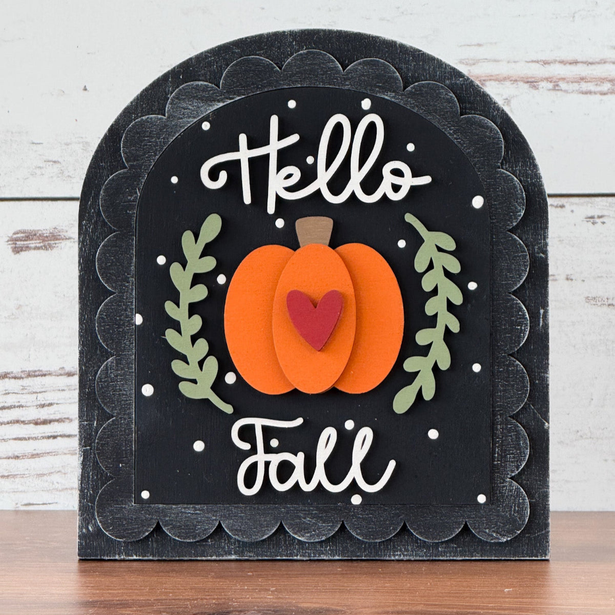 Decorative sign with 'Hello Fall' text and pumpkin design on a wooden surface.