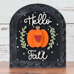 Decorative sign with 'Hello Fall' text and pumpkin design on a wooden surface.