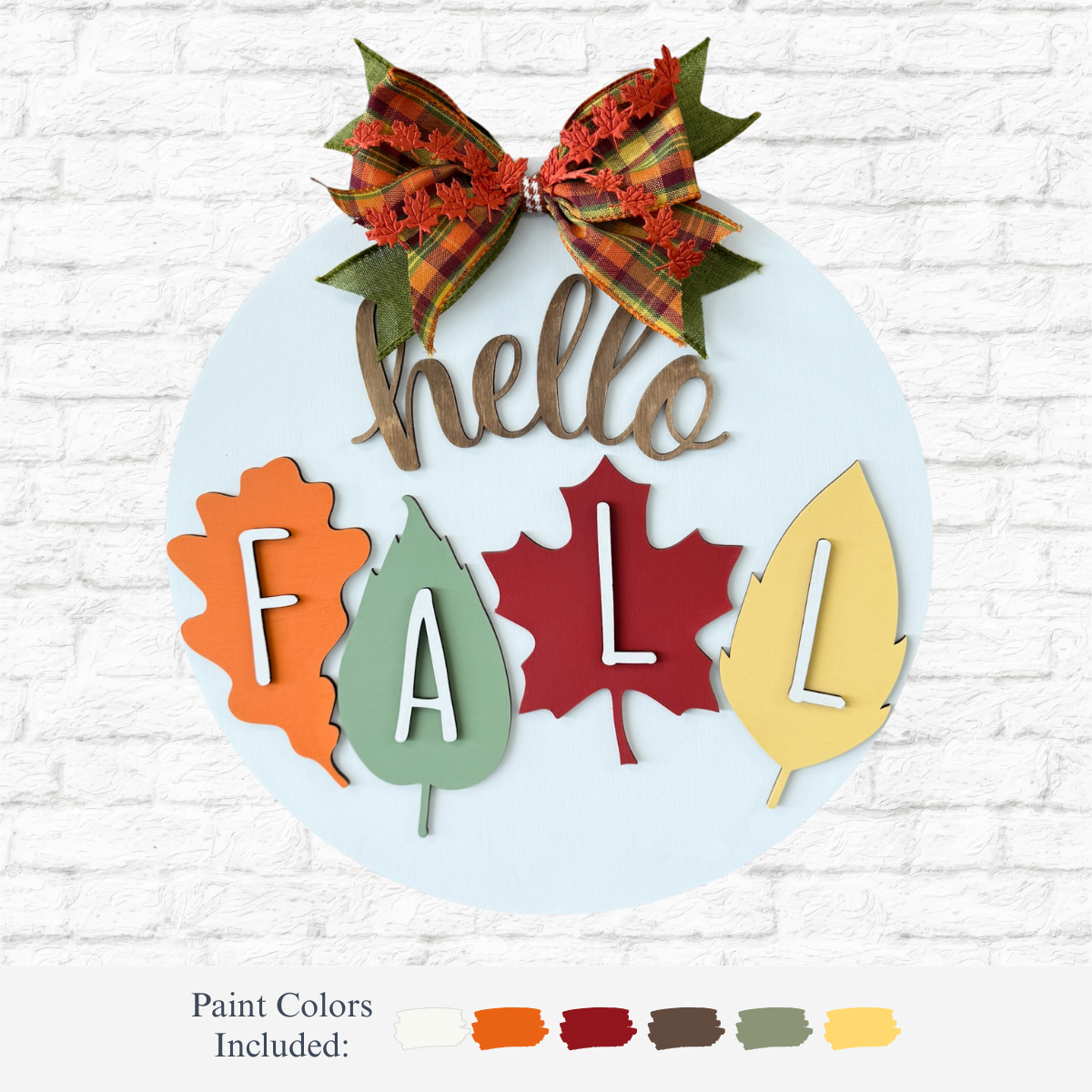 The Rustic Rhode’s DIY Hello Fall Door Hanger kit includes a decorative sign with a plaid bow, “hello,” and leaves spelling “FALL,” plus paint options in orange, cream, green, red, yellow, brown, and gold.