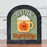 The Rustic Rhode’s DIY Hey There Pumpkin Arch Insert features a mug with whipped cream, a pumpkin design, and playful HEY THERE PUMPKIN text on a green background. This decorative fall sign fits a black scalloped arch insert frame.
