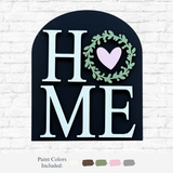 The Rustic Rhode’s DIY Home Arch Insert features “HOME” with a wreath and heart as the O on a black arch. Includes white, beige, brown, green, and pink paints—perfect for adding a cozy touch to your décor.