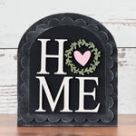 Decorative sign with 'HOME' and heart design on a wooden surface and white wooden background